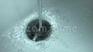 在白色陶瓷脸盆中，一股自来水喷入金属塞子的特写镜头。 水滴和气泡