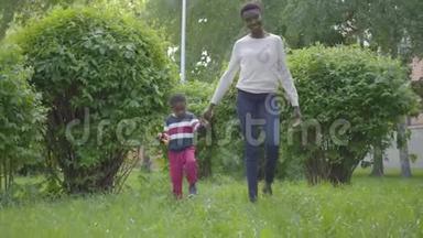 漂亮的非裔美国女人和她的小儿子牵着手在<strong>公园里散步</strong>。 可爱的孩子花时间
