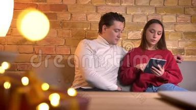 在家庭氛围中，年轻的白种人朋友坐在沙发上专注地与平板电脑合作，特写照片。