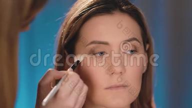 化妆师在眼皮上抹黑，在一个白人金发模特的脸上用专业的白色画笔