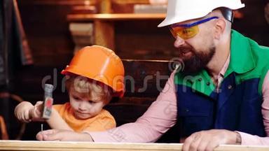 父亲和儿子戴着防护头盔，把钉子钉在木板上。 父亲教他儿子一件建筑事务。