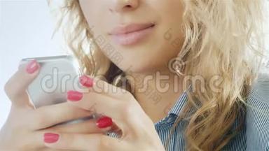 女人在智能手机上打字，微笑着。 特写的手在相框里可以看到用手机和嘴唇合在一起