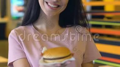 微笑的女人在镜头前展示美味可口的汉堡，肥胖的风险