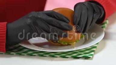 戴黑手套的人吃富含卡路里的快餐汉堡，暴饮暴食