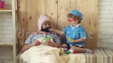 小医生用药片治疗躺在毯子下面的病人. 男孩和他父亲扮演医生。 概念