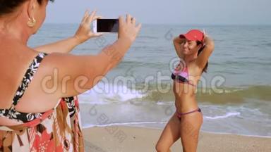 成熟的女人为她晒黑的女儿在海边的泳装上`智能手机拍照