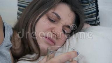 一个怀孕的女孩睡在沙发上，醒来喝了一杯水。 疲惫的孕妇渴望喝一杯