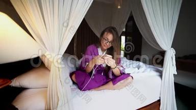 美丽的女人在床上使用手机管理智能连接的家庭移动应用程序