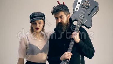 有胡子的男人拿着吉他，一个女人戴着皮帽子，互相看着对方。 有吉他的硬摇滚情侣。 妇女