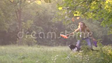 女孩训练者在绿色草坪上投掷橙色飞盘犬在绿色草坪上追逐它，慢动作射击