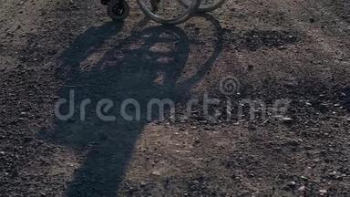 一个轮椅站在一条肮脏的石路上，挡住了一个影子。
