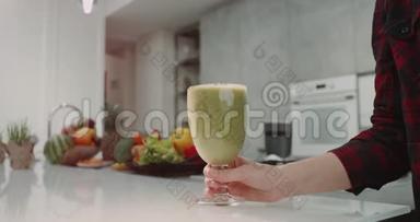 早晨，现代厨房年轻的一家人喝了一杯健康的绿色冰沙，女士端冰沙的杯子，带来