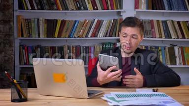 吸引人的成年快乐商人在图书馆里坐在笔记本电脑前的平板电脑上视频通话