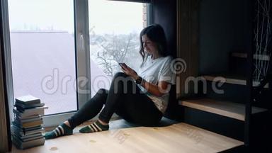 女人坐在窗边，用<strong>手机浏览</strong>社交媒体。 侧视。