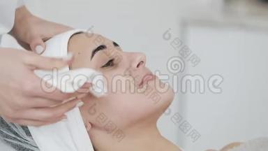 美丽的女人在水疗沙龙按摩她的脸之前，用餐巾擦拭她的脸。 慢动作