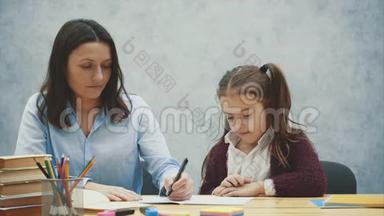 妈妈和女儿<strong>的</strong>灰色背景。 在这期间，她为一个微笑<strong>的</strong>女儿<strong>写作业</strong>。 关系概念。