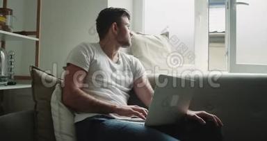 早上在客厅里，男人放松地检查了他坐在沙发上的笔记本电脑。