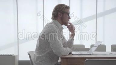 一个戴眼镜的金发体贴的男人坐在桌旁，坐在上网本前一间舒适的办公室里，<strong>抚摸</strong>着他的眼睛