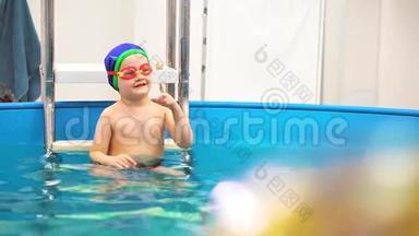 游泳池里一个戴泳镜的小男孩接住了一个蓝色的球。 他抠鼻子