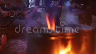 人们用篝火在金属桶里<strong>加热食物</strong>。 一个人在弹吉他，其他人在听他