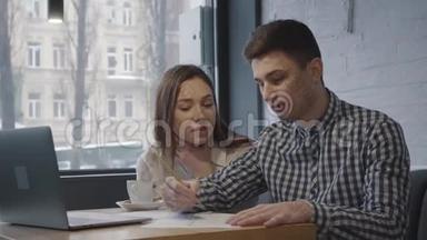 一个年轻人和女孩坐在一张桌子上，在一家舒适的咖啡馆或餐馆的窗户附近有一台笔记本电脑。 朋友