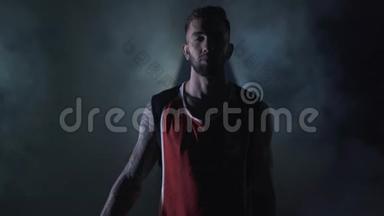 肖像年轻英俊，野蛮，没有编织，自信的篮球运动员站在烟雾缭绕的黑色背景下。