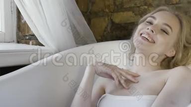 一幅美丽的金发女孩的画像，她穿着白色无肩带上衣，坐在空荡荡的浴室里，笑在红砖墙上