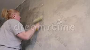 一个女人用滚筒在粉刷墙壁之前对墙壁进行处理。