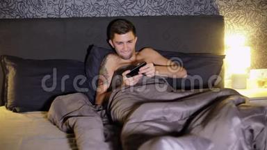 年轻人晚上躺在家里的床上玩智能手机游戏。 紧张的比赛，赢得比赛并且是