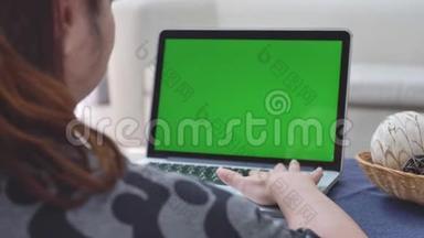 过肩射的亚洲女子看着绿屏.. 办公室人员使用带有笔记本电脑绿色屏幕的笔记本电脑