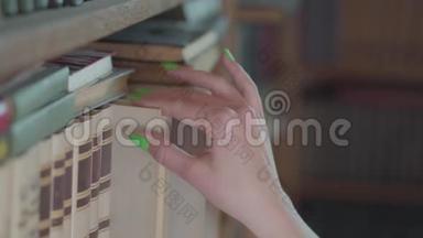 侧视手中的年轻学生与明亮的绿色指甲选择书在图书馆近距离。 女孩