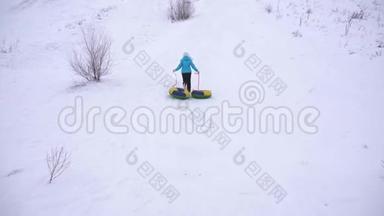 女孩爬上高高的雪山，手里拿着雪碟。 女人在冬天玩雪橇。 山区度假胜地