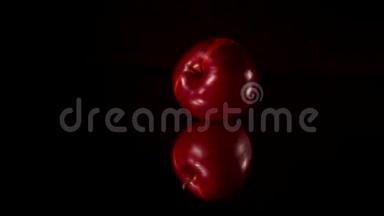 新鲜的红苹果在黑镜桌上旋转滚动。 黑色背景。