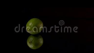 绿色新鲜石灰或绿色柠檬在镜子上的黑色背景上旋转。