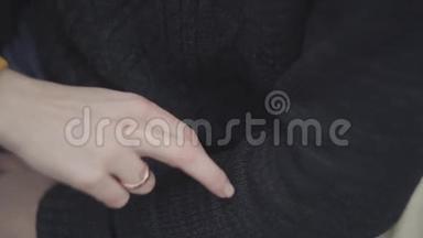 女人的手，她的手指上的金戒指紧闭。 两根手指在穿黑色毛衣的男人的手臂上行走