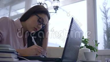 由于学习过度，疲惫的女学生眼镜使用笔记本电脑从网上教学准备考试