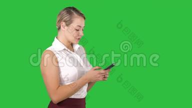 发短信给一个有魅力的年轻女人，她拿<strong>着</strong>智能<strong>手机</strong>，站在绿色的地上微笑<strong>着看着</strong>它
