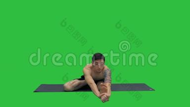 坐着的男人在<strong>绿色</strong>屏幕上，Chroma键，摆出伸展腿和脊柱的姿势。