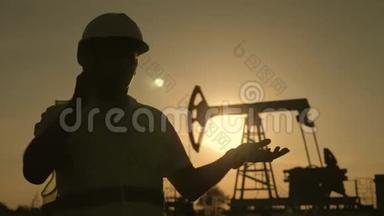 人力工程师剪影，带电话，监督日落时原油生产现场。