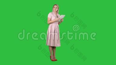 穿着粉红色衣服的女青年女士站着，拿着平板电脑，在绿色屏幕上给相机演讲，Chroma键。