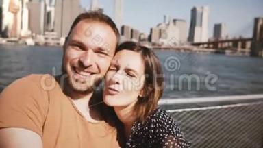 幸福微笑的年轻夫妇摆姿势拍照，亲吻著名的纽约天际线曼哈顿摩天大楼。