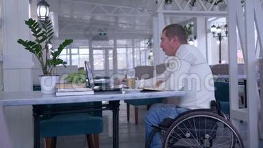 在线课程中，坐在轮椅上的残疾学生使用笔记本<strong>电脑</strong>，<strong>端</strong>着书坐在桌子旁喝咖啡