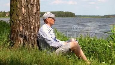 戴帽子的人坐在湖边的一棵树下喝水