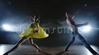 一个男人和一个女人一起跳舞，一个穿着牛仔裤的滑稽舞蹈和一条黄色的裙子在舞台上冒烟。 音乐剧