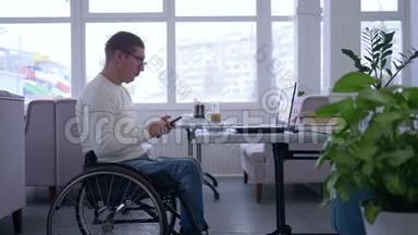 在线学习，自由职业者残疾人在轮椅上戴眼镜使用手机与电脑坐在一起
