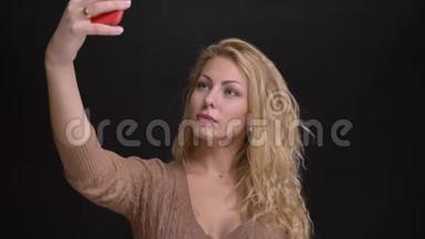 华丽的白种人长发女人在黑色背景下的智能<strong>手机</strong>上<strong>制作</strong>自拍照片的肖像。
