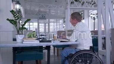 坐在<strong>轮椅</strong>上的<strong>老年</strong>残疾人，端着一杯咖啡坐在桌旁，用手机说话，用手提电脑