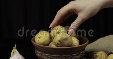 女人手把土豆<strong>一堆一堆</strong>地拿着。 盘子里脏的生土豆