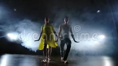 一个男人和一个女人一起跳舞，一个穿着牛仔裤的滑稽舞蹈和一条黄色的裙子在舞台上冒烟。 音乐剧