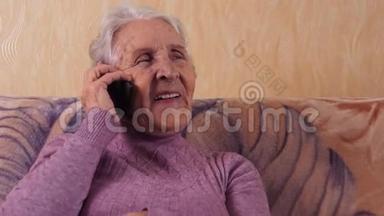 一位坐在沙发上用手机说话的老年妇女。 他通过手机、智能手机进行交流。